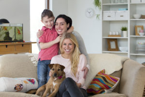 Female couple with son and pet dog posing for the camera in their home